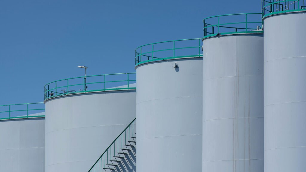 Industrial storage tanks with green railings under clear blue sky, modern infrastructure for oil, chemical, or water storage.