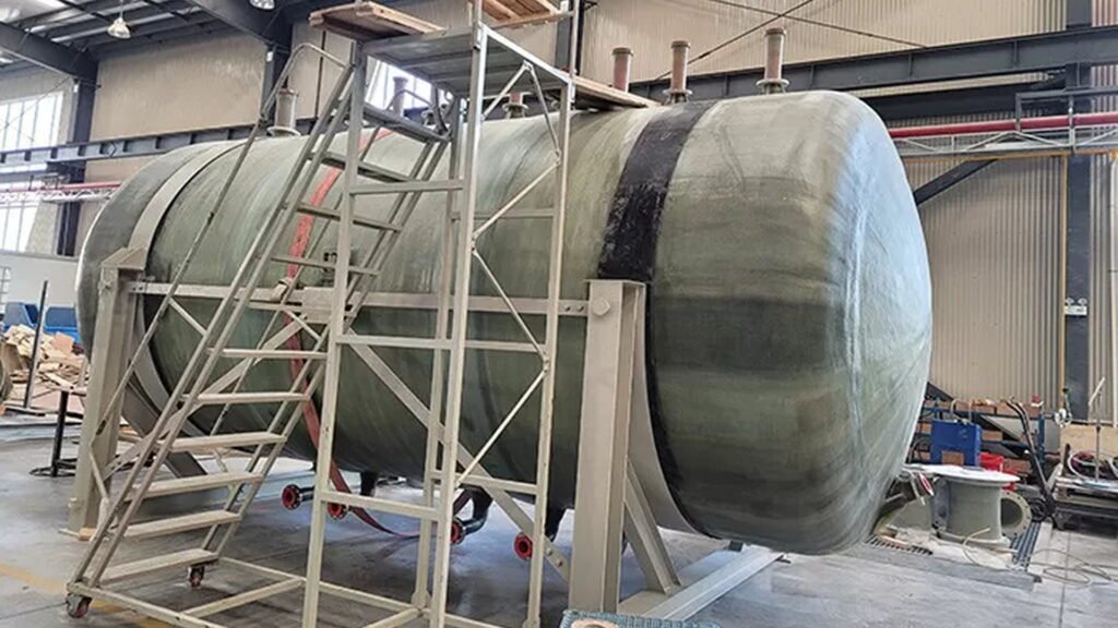 arge FRP storage tank under installation inside industrial workshop.