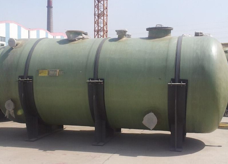 Horizontal cylindrical green FRP (fiber-reinforced plastic) water storage tank with black steel support saddles, designed for above-ground water storage in industrial and commercial applications.